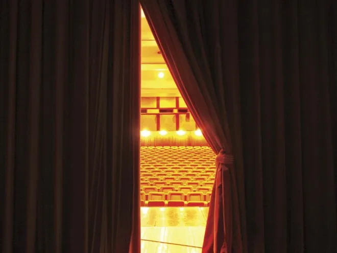 Closed theatre curtains with an opening revealing empty chairs